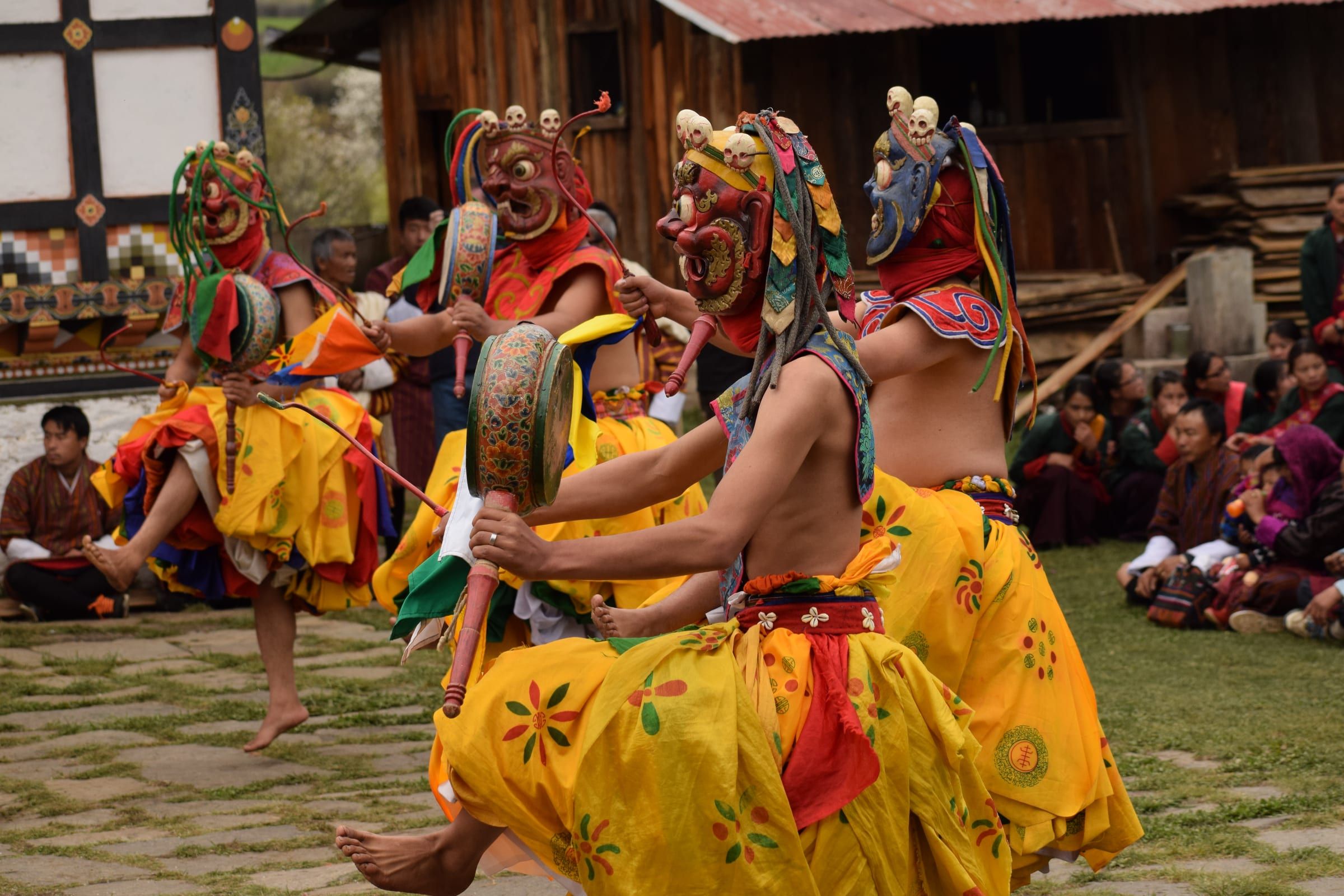 Masked dancers in yellow skirts beat hand drums in a village courtyard.
