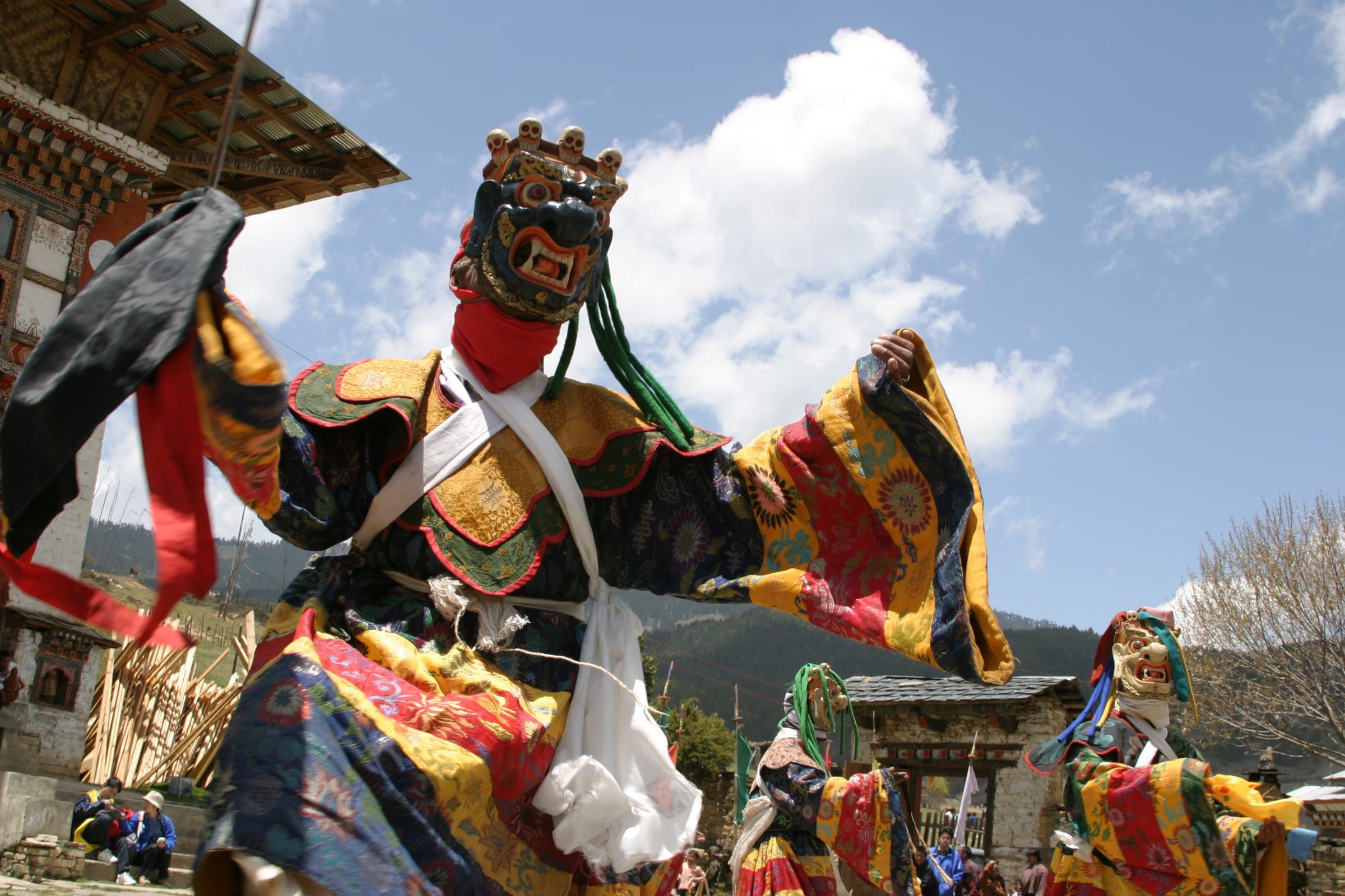 A masked dancer in patterned silk robes leaps against a blue sky.