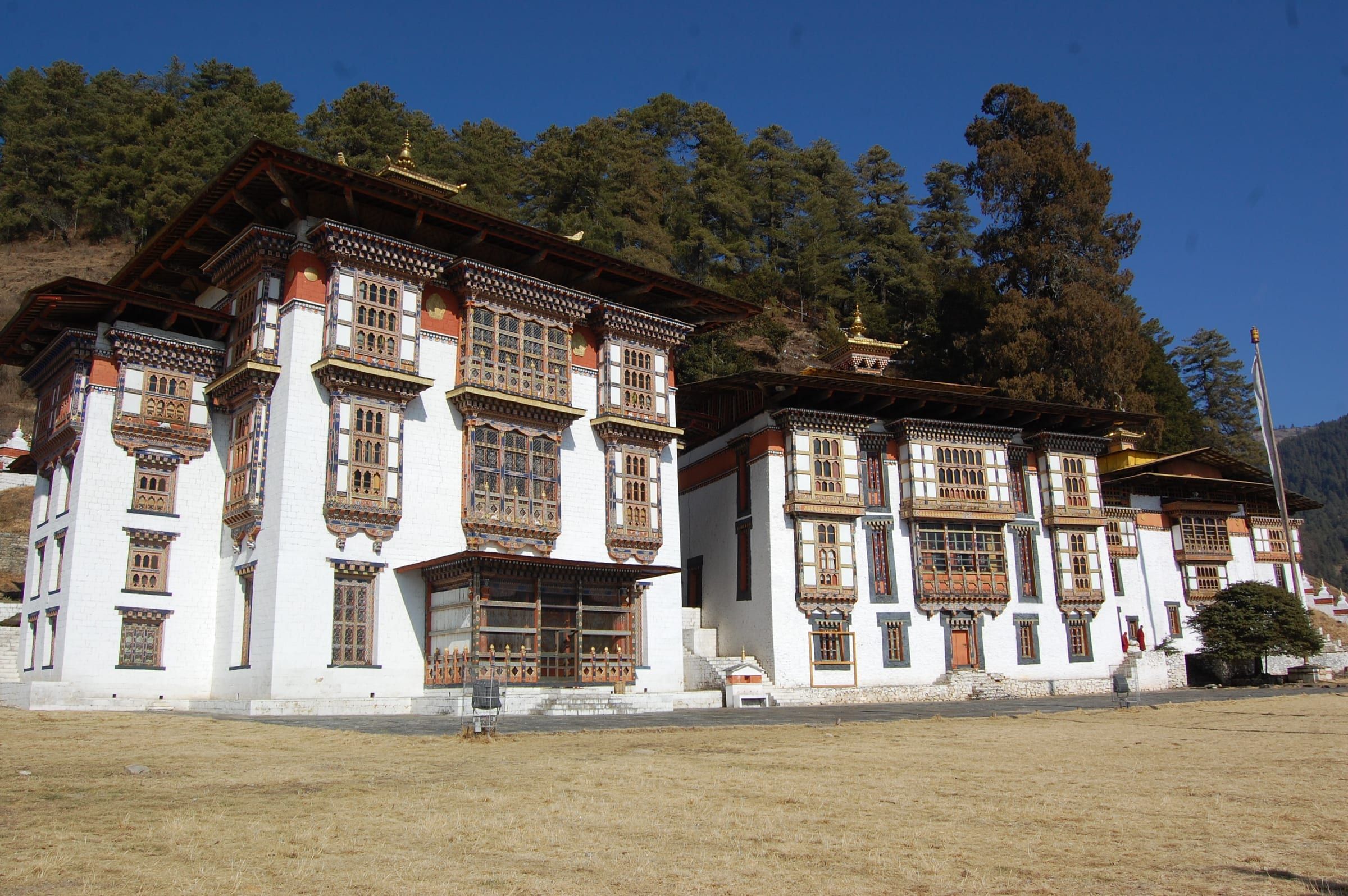 Three whitewashed temples stand side by side below a forested slope.