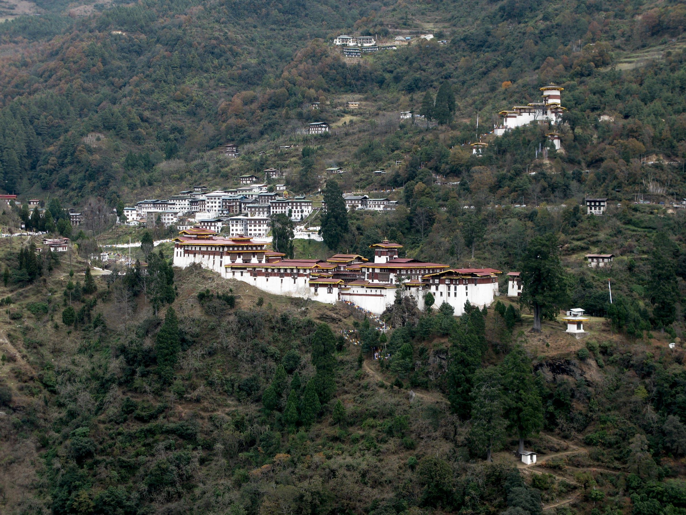 Trongsa Dzong along a forested ridge, with its watchtower on the slope above.