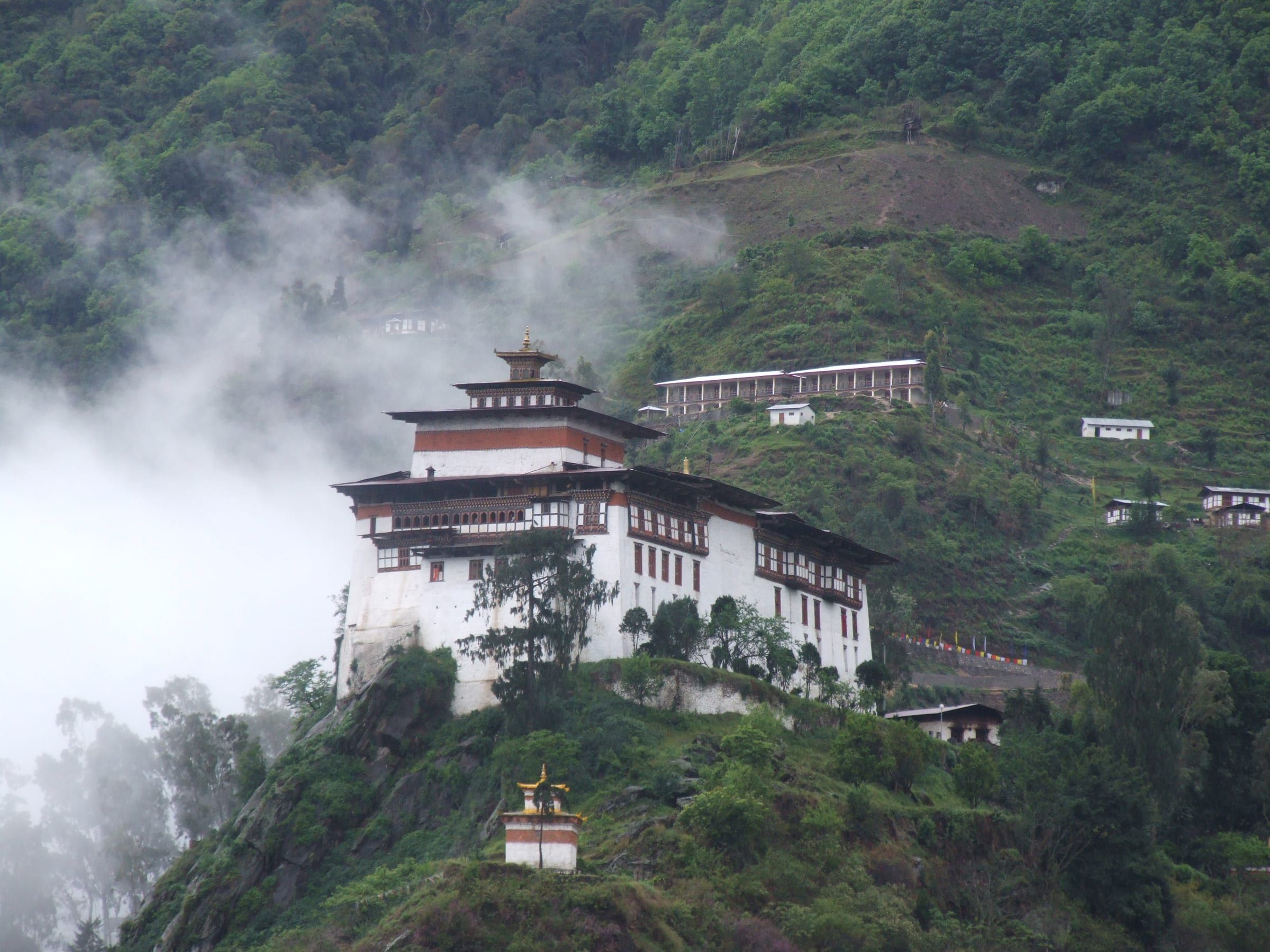 Lhuentse Dzong on a steep spur, with mist drifting across the forest.