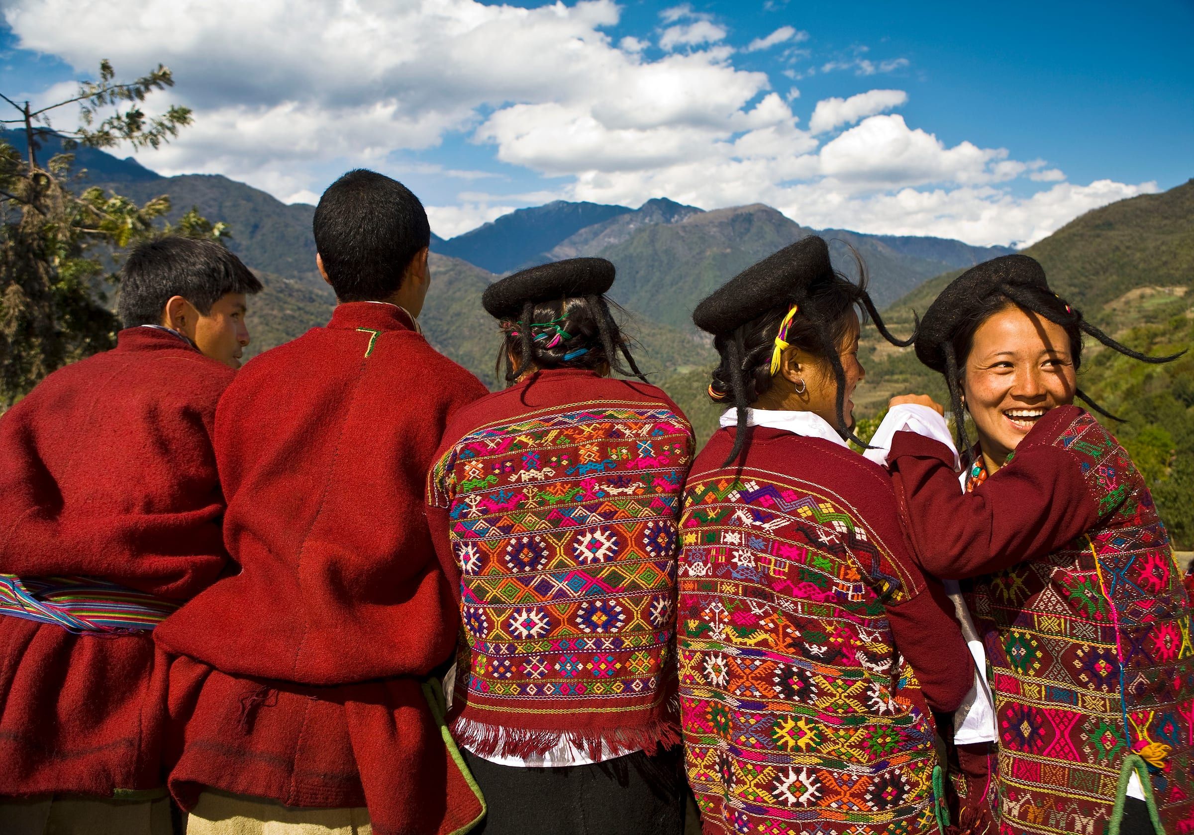 Brokpa men and women in red woollen dress and felt hats look out over mountain ridges.