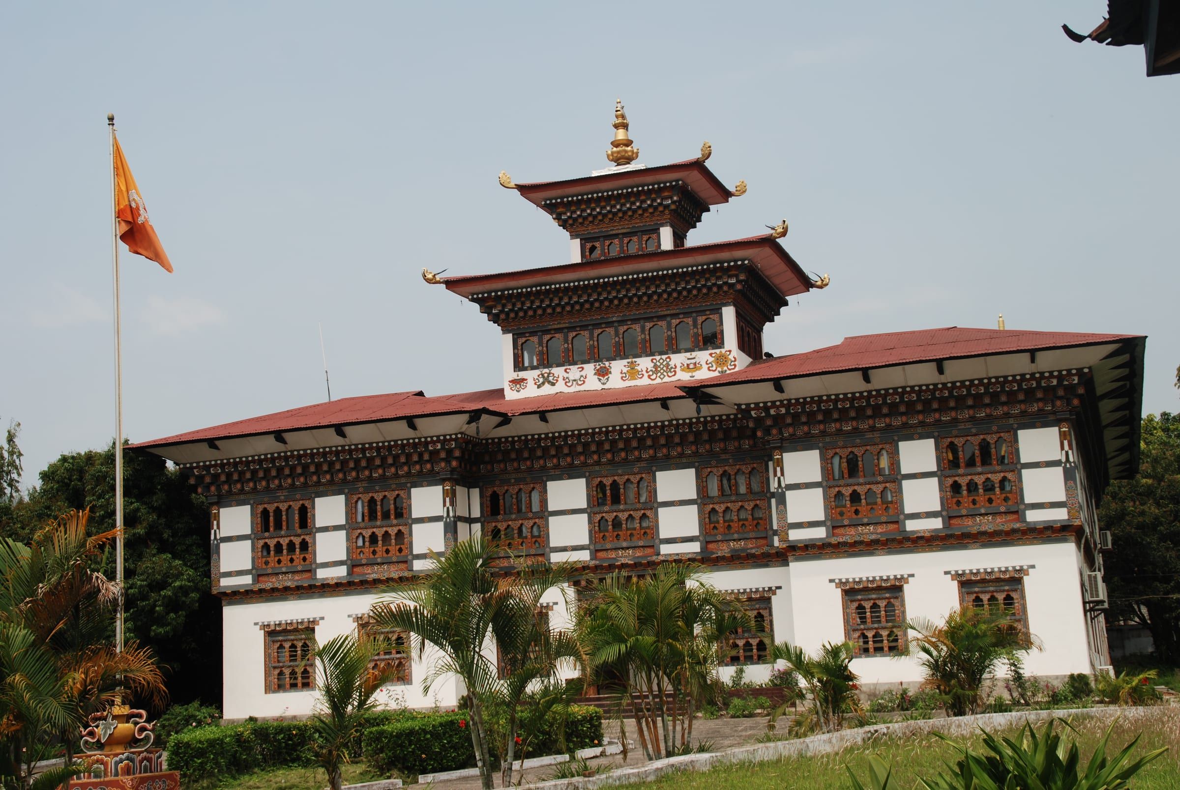 The dzong at Samdrup Jongkhar framed by palm trees, with a flag in front.