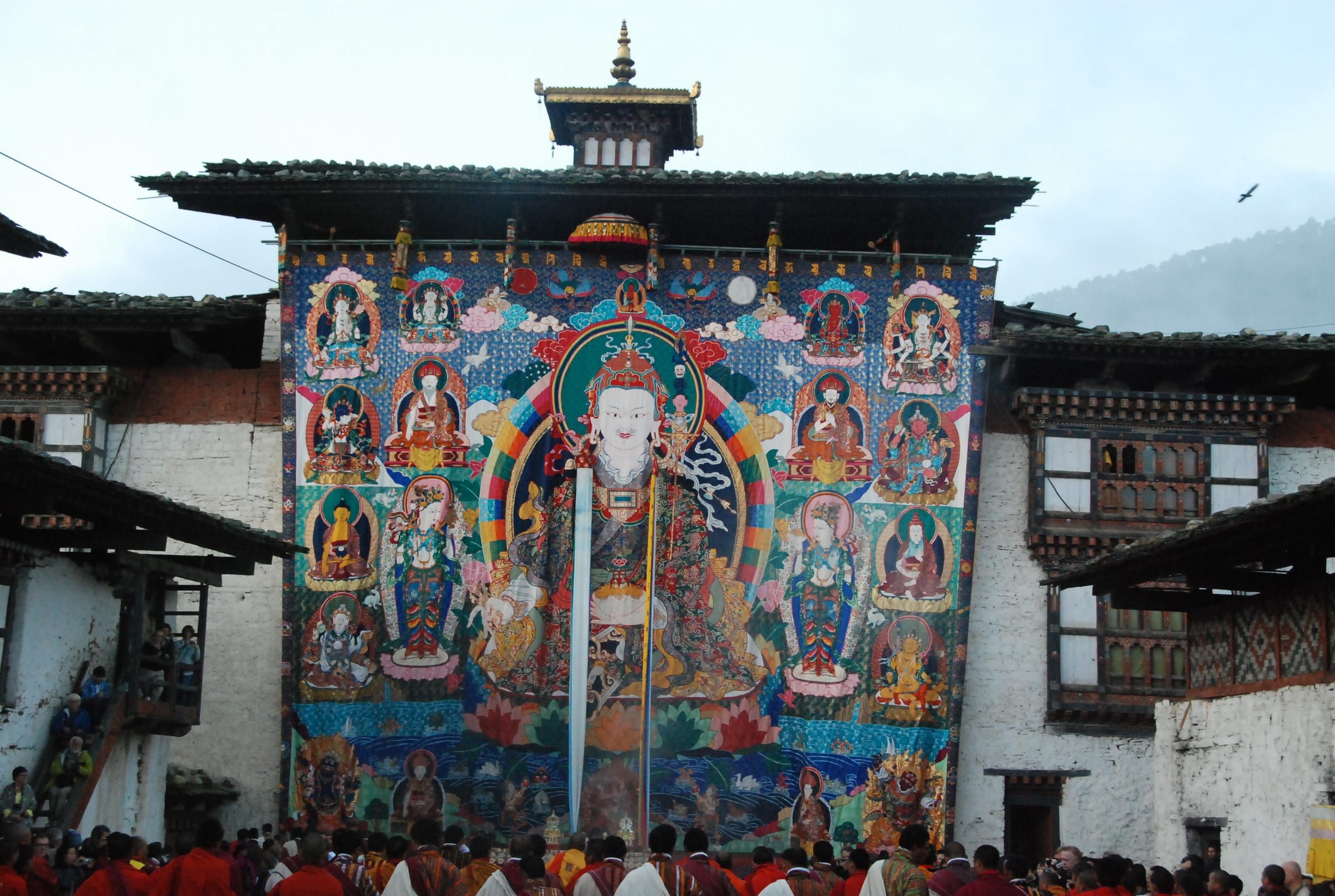 A giant thongdrel of Guru Rinpoche hangs down a temple wall above the crowd.
