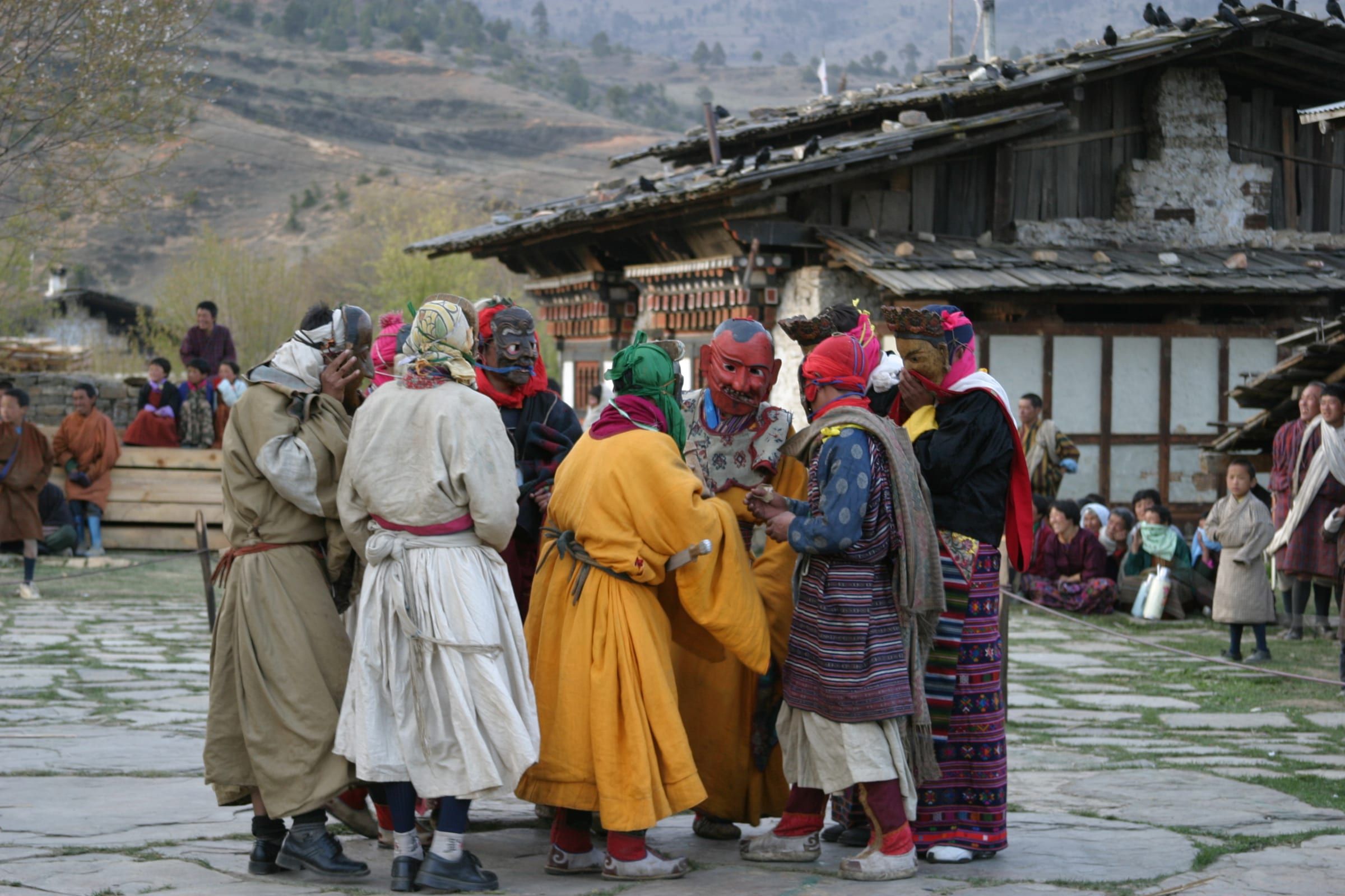 Masked and costumed performers gather in a stone-paved village courtyard.