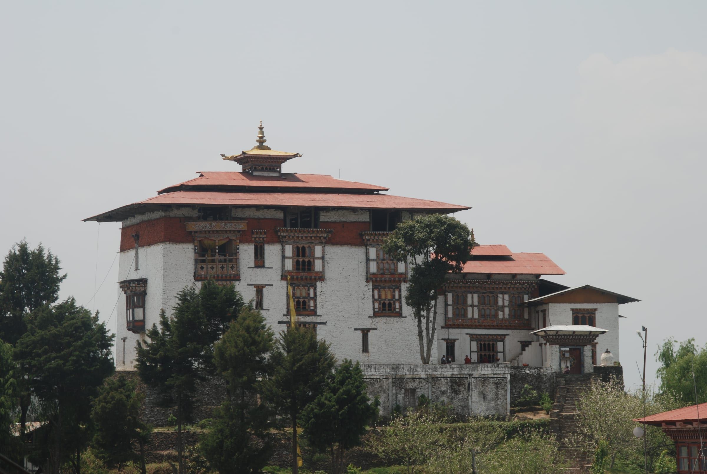 A whitewashed dzong with a golden spire on a hillside above stone steps.